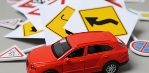 A small red toy car surrounded by scattered miniature traffic signs on a flat surface