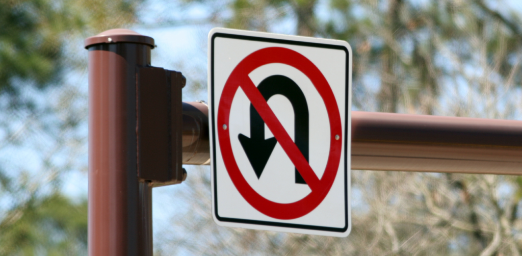 No U-turn road sign mounted on a brown pole, warning drivers of restricted turning areas and helping prevent traffic violations at intersections