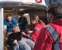 Paramedics helping a patient on a stretcher into the back of an ambulance, indicating an emergency situation