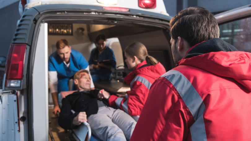 Paramedics helping a patient on a stretcher into the back of an ambulance, indicating an emergency situation