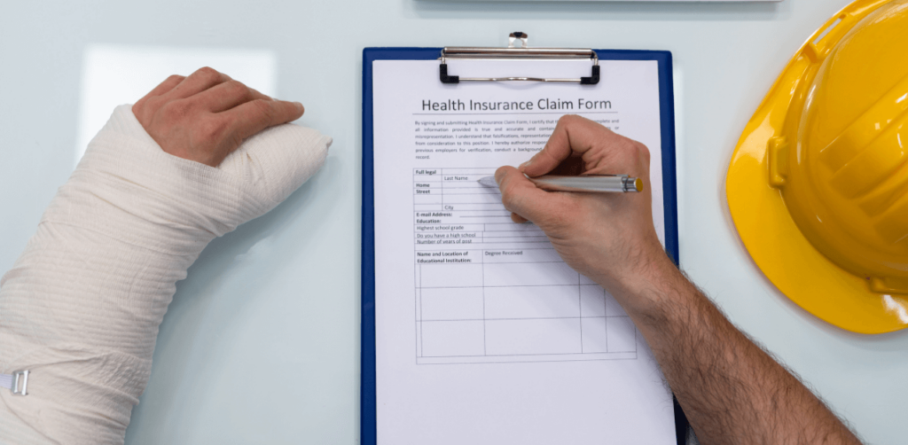 Person with a bandaged arm filling out a health insurance claim form, with a yellow hard hat nearby, indicating a work-related injury