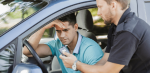 Police officer holding a breathalyzer for a concerned driver sitting in his car