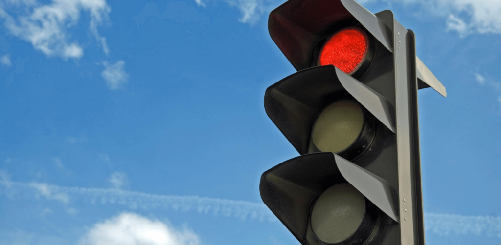 Red traffic light illuminated against a blue sky, signaling vehicles to stop