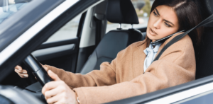 Woman driving while holding a phone between her ear and shoulder, appearing distracted