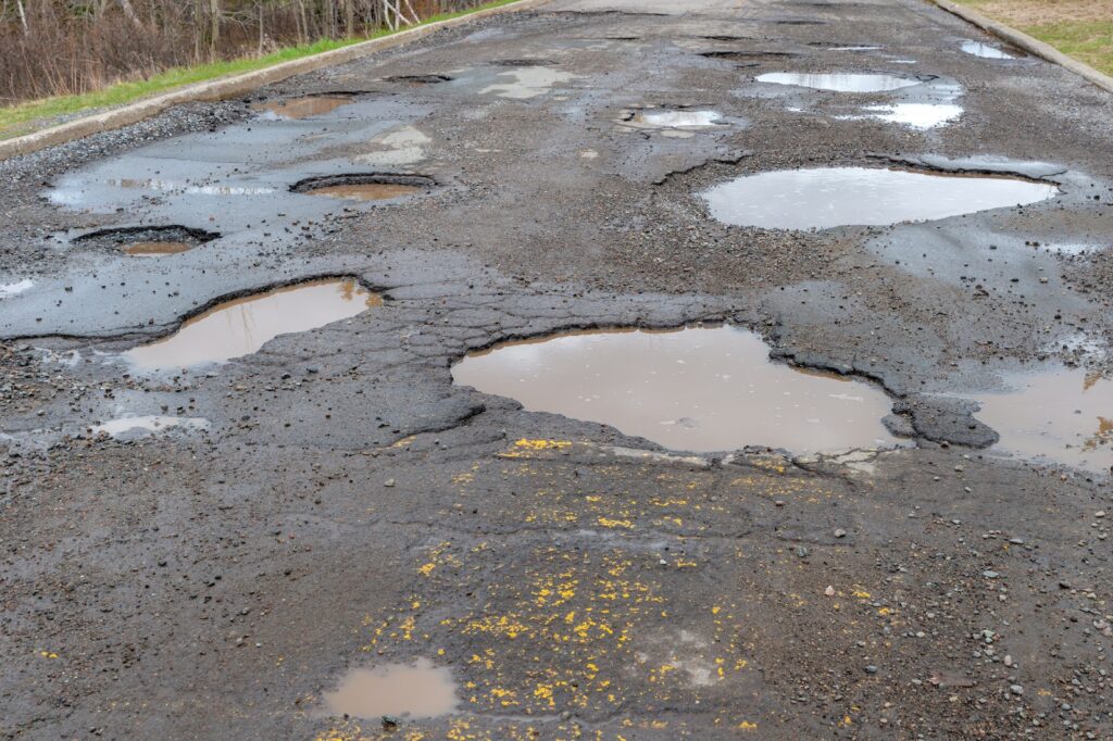 Road with multiple large potholes filled with water, showing significant wear and damage