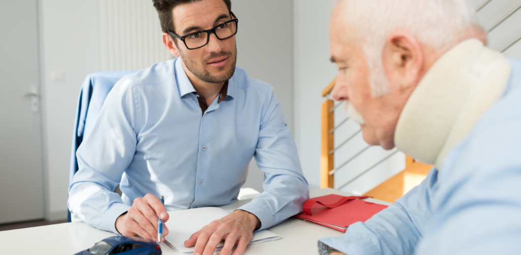A man with glasses and a pen discusses paperwork with an elderly man wearing a neck brace, suggesting a consultation or legal advice after an injury