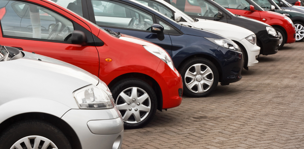 A row of parked cars in various colors, lined up at a dealership or parking lot