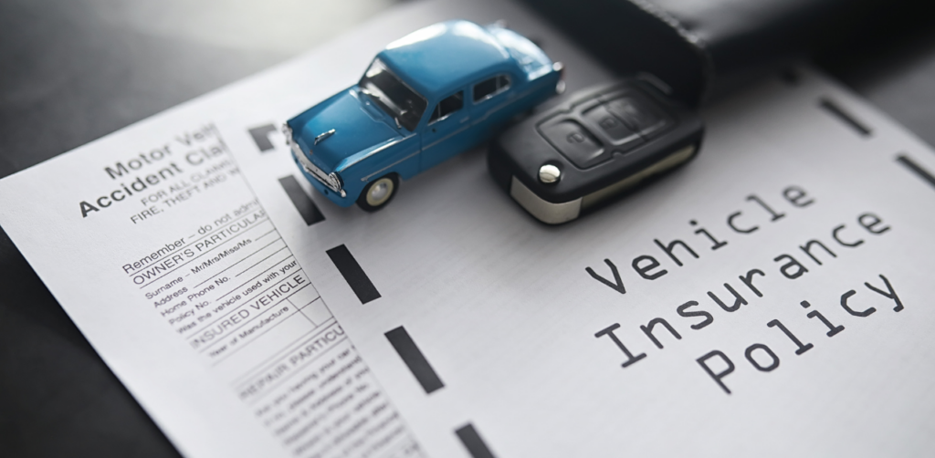 A vehicle insurance policy document with a toy car, car keys, and an accident claim form placed on top