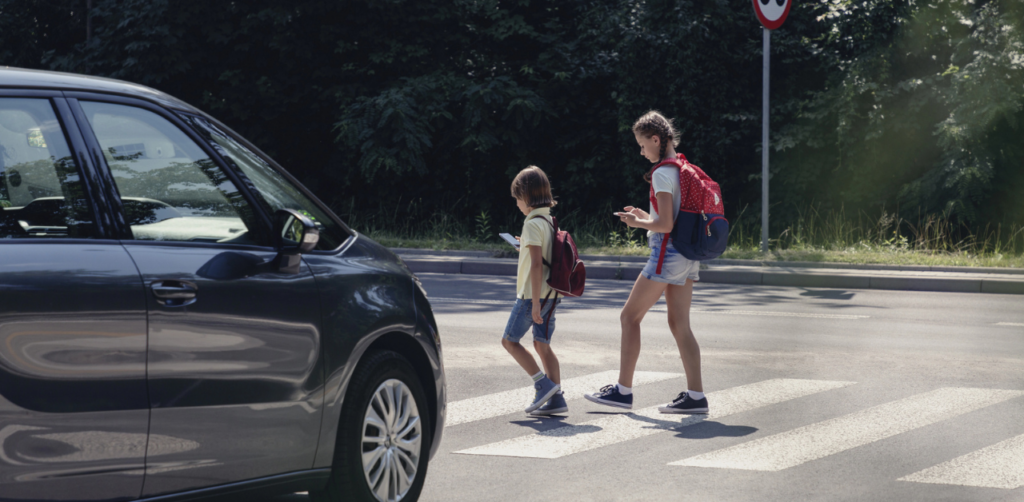 Two children with backpacks crossing the street at a crosswalk as a car waits nearby