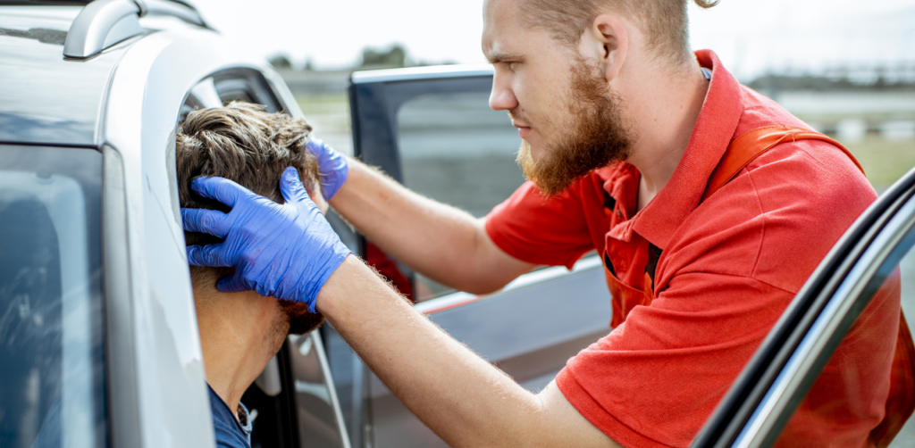 A first responder in blue gloves examines a man's head while he is seated in a car, possibly assessing an injury