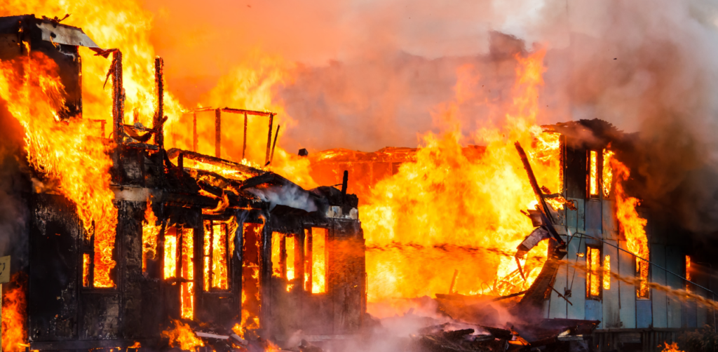 A large building engulfed in flames, with intense fire spreading through its structure