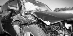 Black and white image of a car with significant front-end damage and a shattered windshield