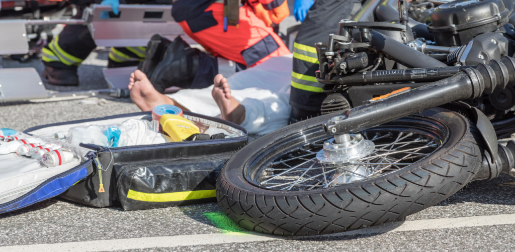 Emergency responders assisting an injured person next to a fallen motorcycle and an open medical kit on the road