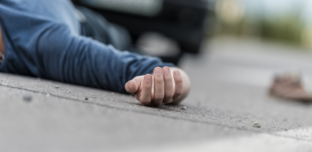 Close-up of a person's hand lying motionless on a road, suggesting an accident or injury