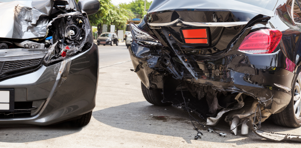 Two cars with severe rear-end damage on a sunny street, showing crumpled bumpers and exposed internal car parts