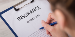 Person filling out an insurance claim form on a clipboard with a pen, emphasizing the claims process