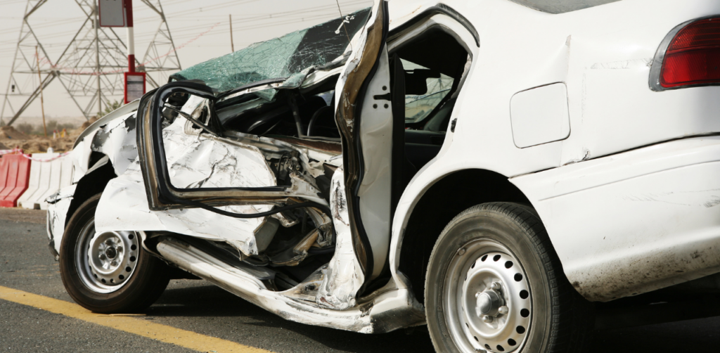 Heavily damaged white car on roadside after a collision, highlighting the need for legal assistance in personal injury cases