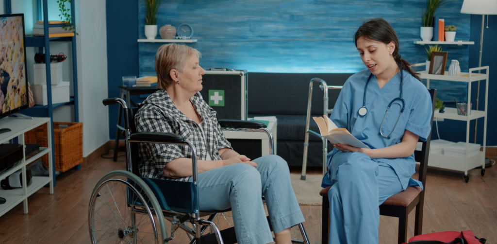 Nurse reads book to older woman in wheelchair, creating a calm moment in a well-lit care facility