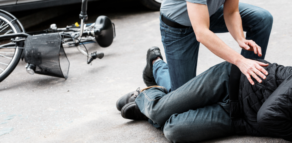 Man giving first aid to injured cyclist lying on the road