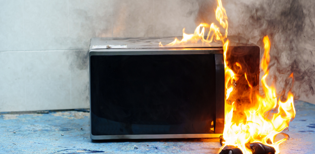 Microwave engulfed in flames on a kitchen floor, showing the aftermath of a dangerous appliance fire