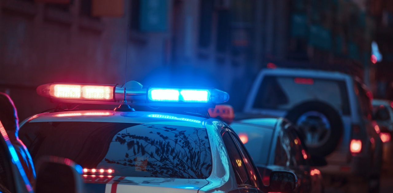 Police car with flashing red and blue lights in city traffic at dusk