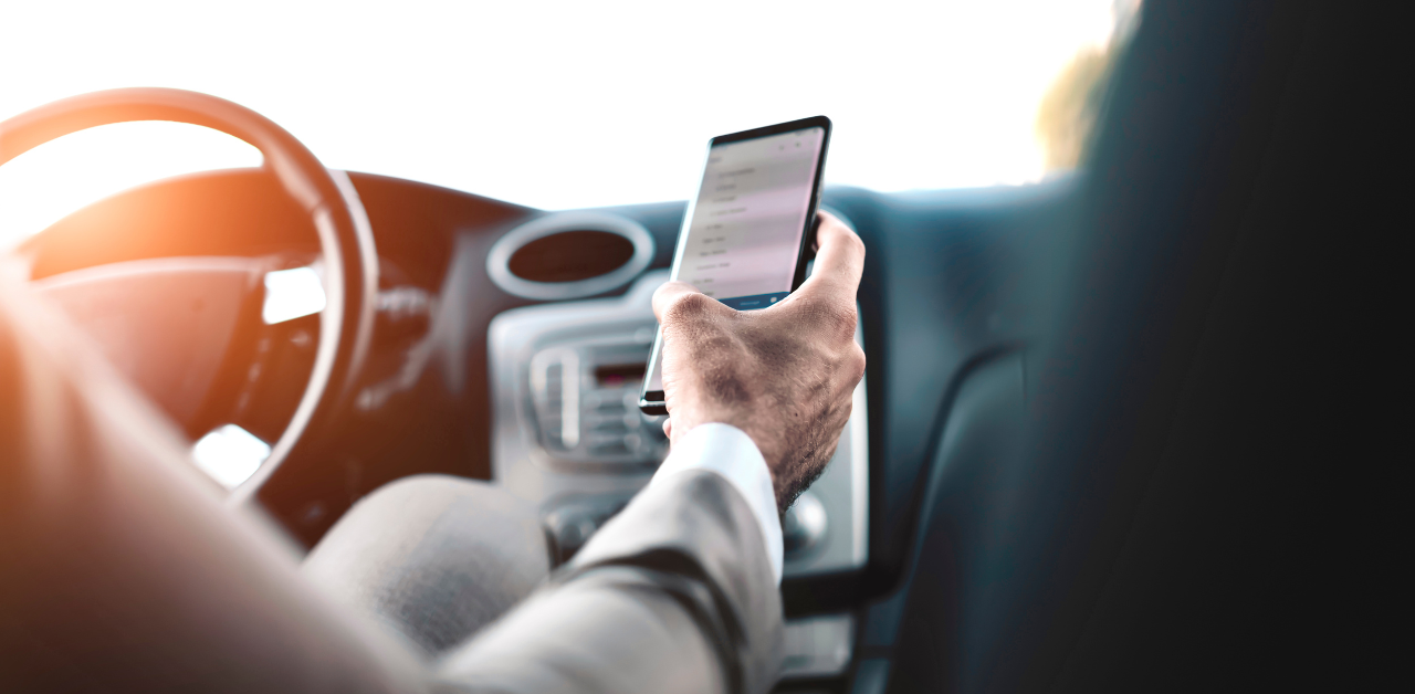 Driver uses a smartphone behind the wheel, illustrating the danger of distracted driving