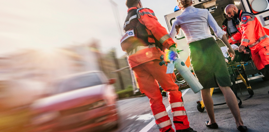Paramedics assist a woman with oxygen near an ambulance after a traffic accident, emergency in progress