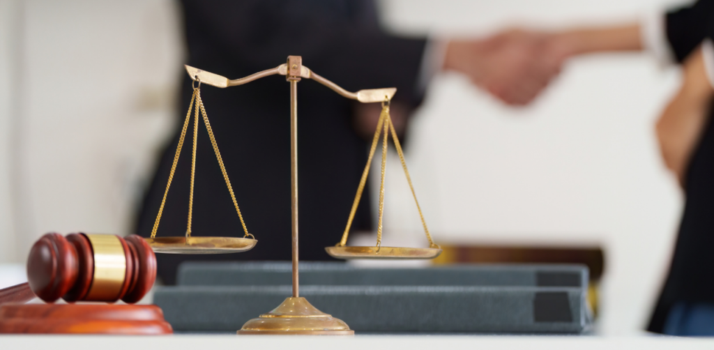Scales of justice and gavel on a desk with two people shaking hands in the blurred background