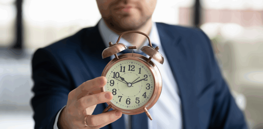 Businessman in a navy suit holding a copper-colored alarm clock towards the camera