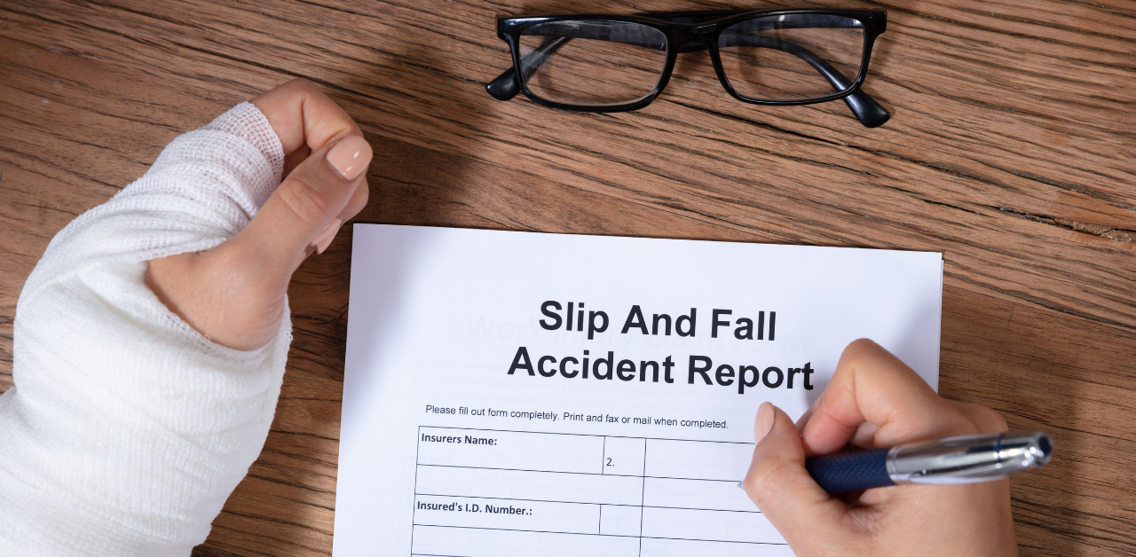 Close-up of a person with a bandaged wrist filling out a “Slip and Fall Accident Report” form on a wooden desk