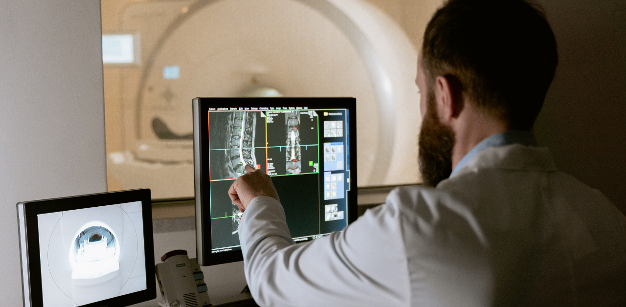 Doctor examining spinal MRI scans on a computer monitor next to an MRI machine
