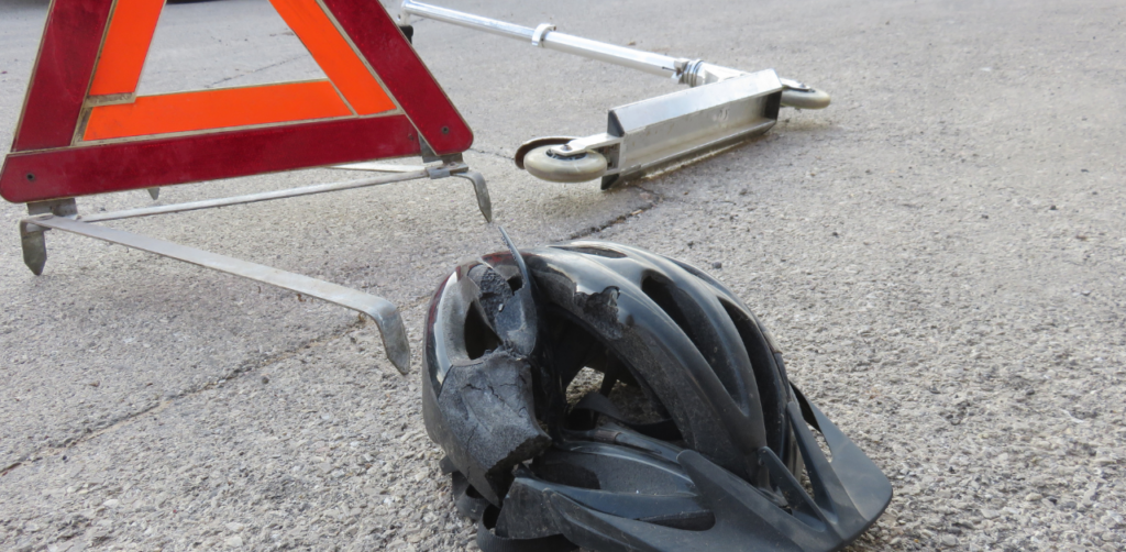 Broken helmet and fallen scooter near warning sign, illustrating electric scooter accident and the importance of safety gear