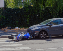 Car and fallen motorcycle after collision at intersection, illustrating road accident, vehicle damage, and traffic safety risks