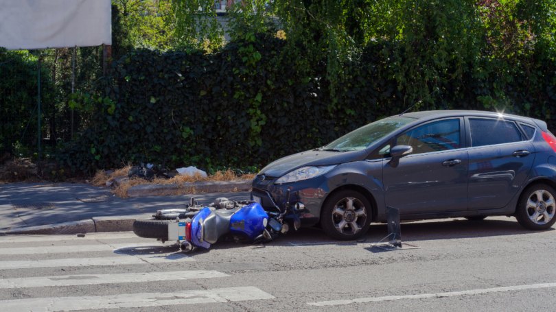 Car and fallen motorcycle after collision at intersection, illustrating road accident, vehicle damage, and traffic safety risks