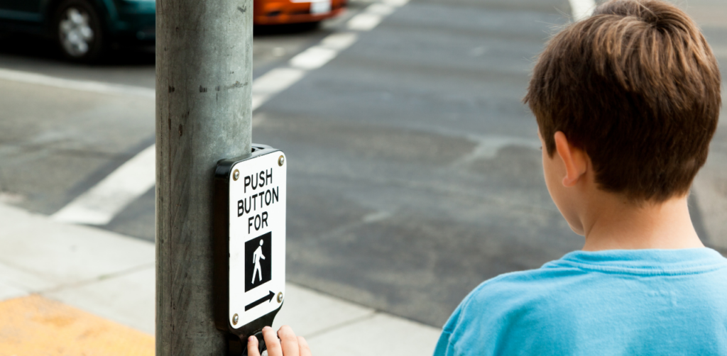 Child pressing pedestrian crossing button at street corner, highlighting road safety and safe street crossing awareness