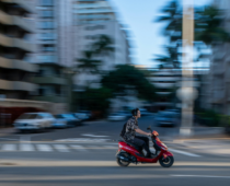Person riding a red scooter through a city street with motion blur, representing fast urban commuting and mobility