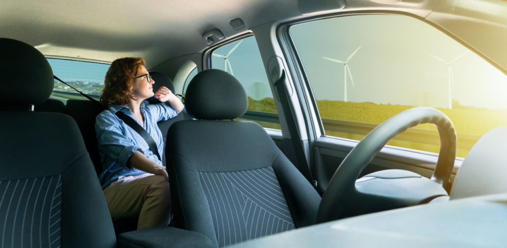 Woman seated in a car looking out the window at wind turbines, reflecting on sustainable energy during a scenic drive