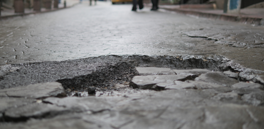 Close-up of a damaged roadway with a large pothole and broken pavement in the middle of a street