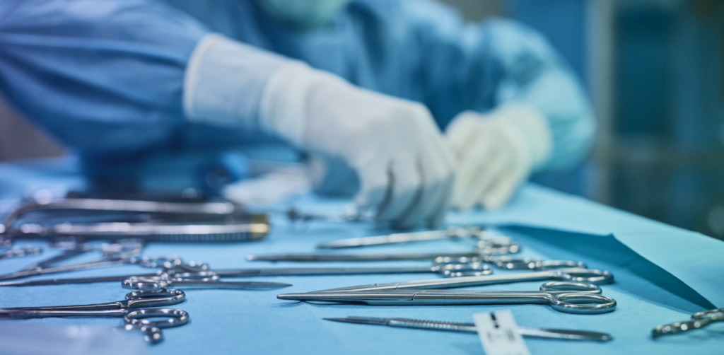 Surgical instruments arranged on a sterile operating table while medical staff wearing gloves prepare in the background