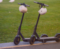 Two electric scooters with helmets hanging from the handlebars parked beside a grassy area