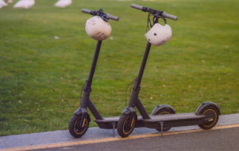 Two electric scooters with helmets hanging from the handlebars parked beside a grassy area