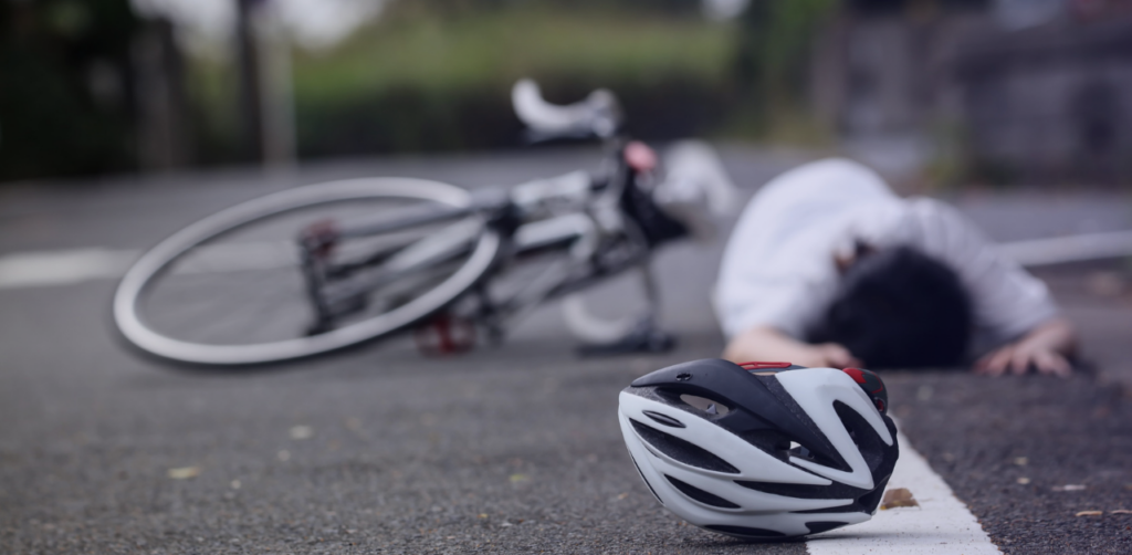 Bicycle helmet in the foreground with a fallen cyclist and bicycle blurred in the background