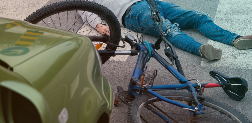 Damaged bicycle lies beside a car after a collision, with an injured cyclist on the road