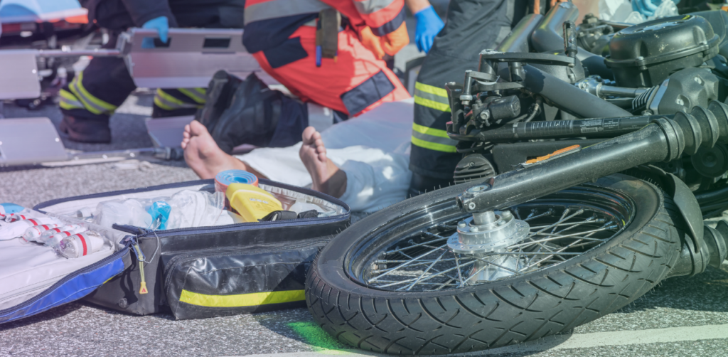 Emergency responders treat an injured person beside a motorcycle after a crash