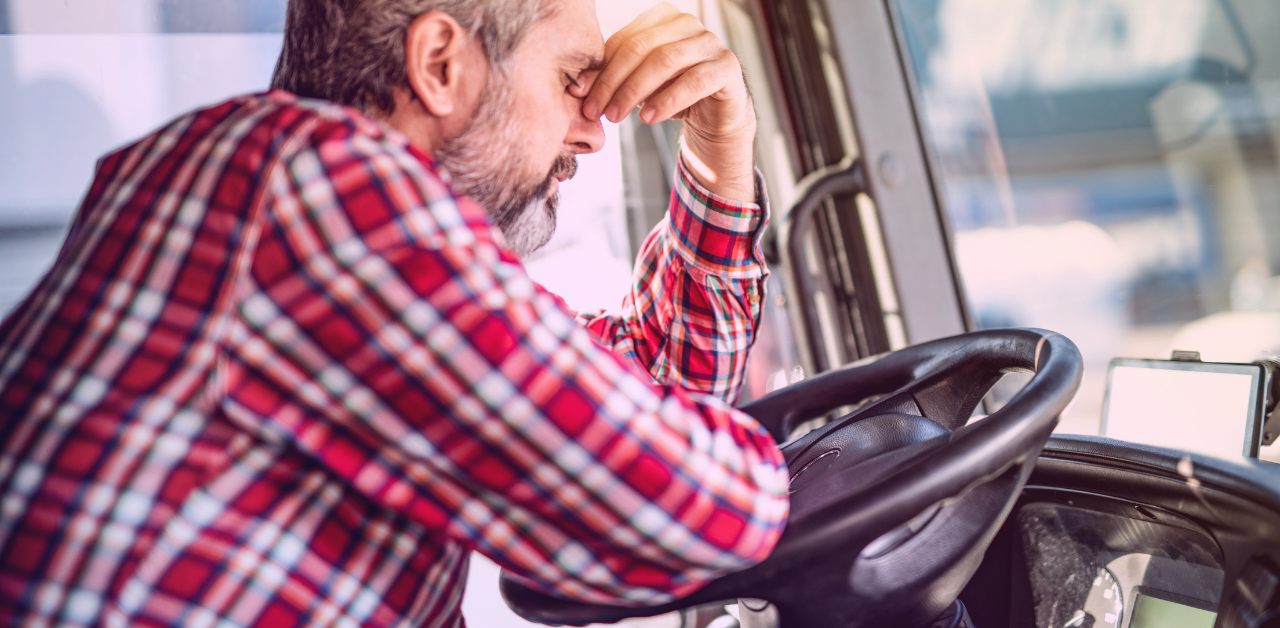 Tired truck driver rests their head on one hand behind the steering wheel