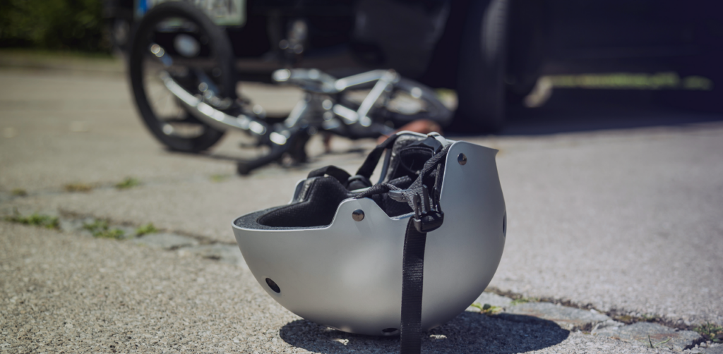 Bicycle helmet lies on the pavement with a fallen bicycle and vehicle blurred in the background