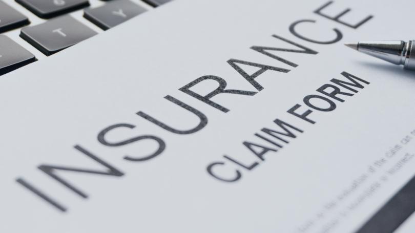 Close-up of an insurance claim form with a pen and computer keyboard in the background