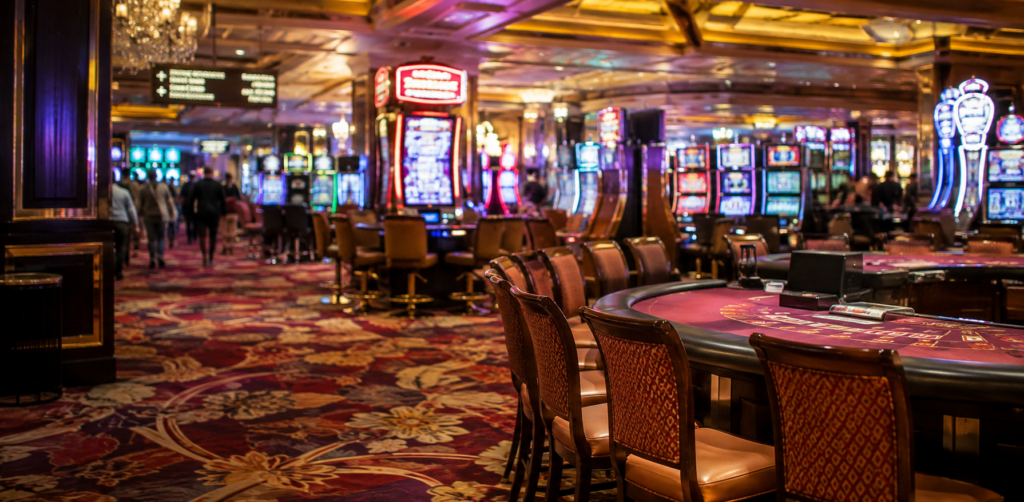 Slot machines and gaming tables fill an ornate casino interior illuminated by chandeliers and colorful displays
