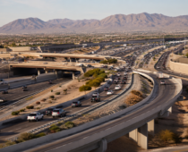 Wide aerial view of intersecting freeways, ramps, and flowing traffic surrounded by desert neighborhoods and mountains